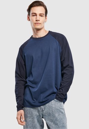 Langarm-T-Shirt mit einem einfarbigen dunkelblauen Körper und dunkleren marineblauen Raglanärmeln. Hergestellt aus weichem Baumwollstoff und mit einem Rundhalsausschnitt gestaltet.