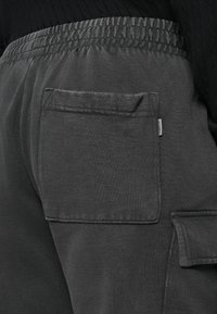Grå bomulds cargo bukser med en sidelomme, elastisk talje og struktureret stof. Nærbillede fra bagsiden.
