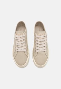 Beige canvas sneakers with round toe, laced design, and textured rubber sole. Subtle logo on the insole, smooth fabric finish.