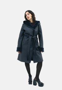 Navy leather wrap coat with a fur-lined hood and sleeves, belted waist, and two front pockets. Smooth texture with a structured design.