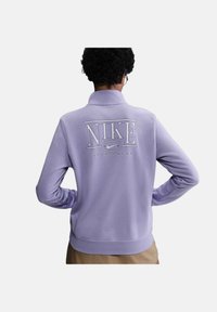 Felpa Nike viola con colletto alto, caratterizzata da un grande logo bianco "NIKE" e dal testo "SPORTSWEAR" sul retro, realizzata in tessuto morbido.