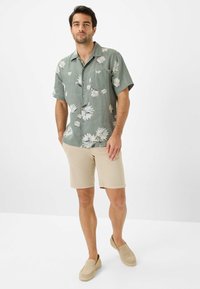 Kurzärmliges, grünes Blumenhemd mit einer Tasche, kombiniert mit beigen Shorts und hellen Slippern. Lässiges Outfit mit einer lockeren Passform.