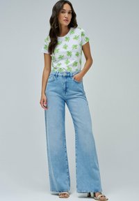 Camiseta blanca con patrón de hojas verdes, combinada con jeans de pierna ancha en azul claro. Tejido suave, corte casual y acentos mínimos en hardware.