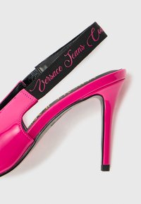 Sapata de salto alto em pele sintética fúcsia com design slingback, apresentando uma tira preta com o texto rosa "Versace Jeans Couture".