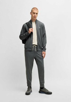 Grijze zip-up jas met hoge kraag, gecombineerd met bijpassende grijze joggers, beide met een gladde textuur en subtiele ontwerpdetails.
