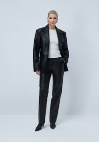 Black leather blazer with notched lapels, paired with matching tailored pants. Model wears a white fitted top and pointed black heeled boots.