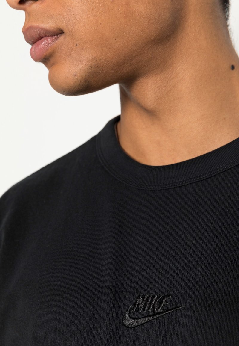 Schwarzes Baumwoll-T-Shirt mit rundem Ausschnitt und einem dezenten, schwarz gestickten Nike-Logo auf der Brust. Weicher Stoff, lässige Passform.
