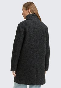 Manteau en mélange de laine gris foncé avec un col montant, des manches longues et une coupe légèrement oversize texturée. La vue de dos montre des détails de coutures.