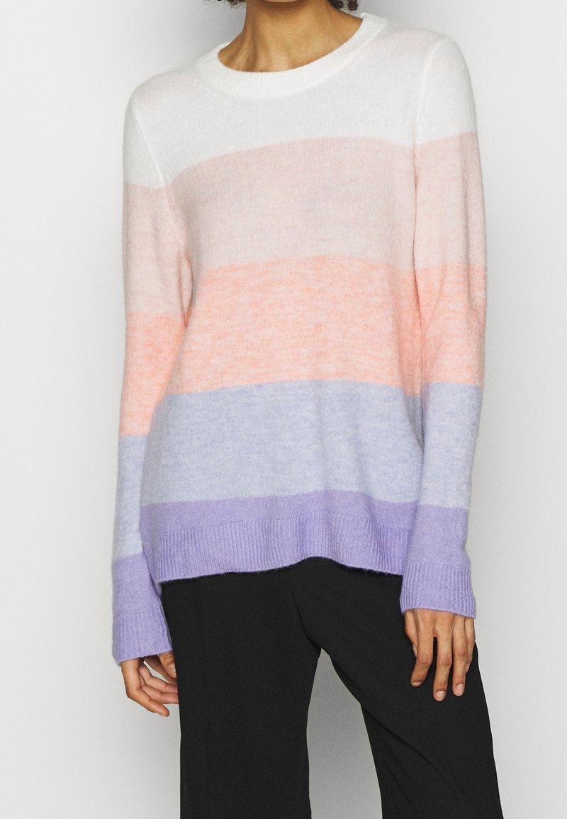Striped sweater in white, pink, lavender, and purple shades. Soft texture, crew neckline, and ribbed cuffs. Paired with black trousers.
