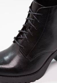 Bottine noire en cuir avec bout rond, lacets à l'avant et semelle épaisse, montrant des coutures détaillées et une texture lisse.
