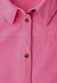 Chemise en velours côtelé rose avec col pointu et trois boutons marron sur le devant au centre.