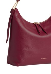 Bordeaux leren schoudertas met een zachte textuur, gouden hardware en een ritsluiting. Heeft een gestroomlijnde, gebogen vorm.