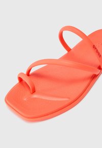 Sandale plate corail vif avec trois fines lanières, dont une boucle pour les orteils, et une semelle légèrement texturée.