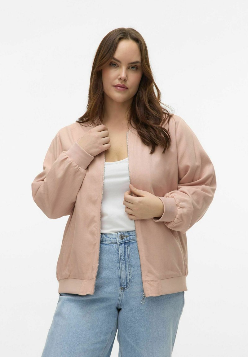 Lys pink bomberjakke med lynlås foran, ribbede manchetter og et afslappet design, parret med lyseblå højtaljede jeans. Glat tekstur.