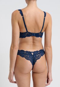 Marinblå spets-bralette och stringset med scallopade kanter, blommönster, justerbara axelremmar och ett hak-och-öga-stängning baktill.