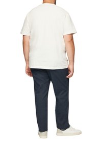 T-shirt blanc à manches courtes, en coton, coupe classique, associé à un pantalon bleu marine et des baskets blanches, vu de dos.