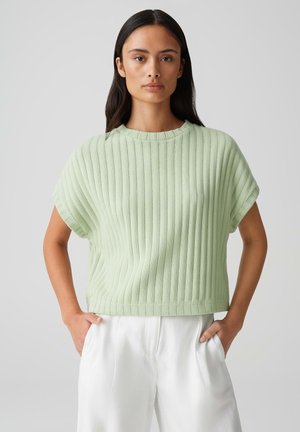 Top corto a maniche corte in maglia a coste verde chiaro, con scollatura rotonda e vestibilità comoda, abbinato a pantaloni bianchi. La texture è morbida ed elastica.
