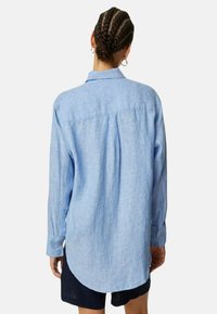 Camisa de manga larga azul claro, mezcla de lino, con cuello, puños abotonados, dobladillo curvado, textura sutil y detalle de pliegue en la parte trasera.