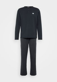 Camiseta de algodón negra de manga larga con un cuello tipo henley abotonado, combinada con pantalones de pijama negros con un diseño geométrico sutil.