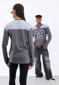 Langermede skjorter i grått med en lys grå øverste del. Den ene har et "69" trykk, mens den andre har en glatt tekstur og en tettsittende design.