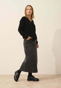 Schwarzer Strickpullover mit V-Ausschnitt, kombiniert mit einem langen grauen Jeansrock und schwarzen Schnürschuhen. Einfaches Design, lässige Passform.