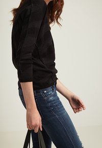 Svartrandig långärmad tröja med en strukturerad stickning, i kombination med blå skinny jeans. En svart tygväska hålls i högra handen.