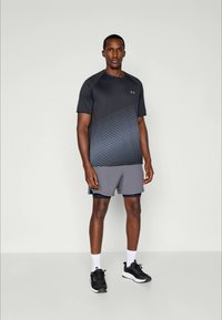 Männliches Sportoutfit bestehend aus einem dunkelgrauen Kurzarmhemd mit diagonalen Streifen und grauen Shorts, ergänzt durch schwarze Sneaker und weiße Socken.