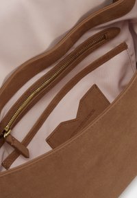 Brown suede bag interior with a smooth, light pink lining. Features a zippered pocket and a small logo tag.