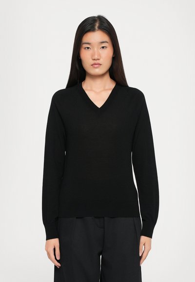 Crni pulover s v-neck izrezom i dugim rukavima, izrađen od glatkog materijala. Prilagođenog kroja s rebrastim detaljima na manžetama i rubu.