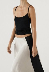 Zwarte, aansluitende tanktop met dunne bandjes, gecombineerd met een vloeiende rok met een zwart zijpaneel en een lichte stof. Soepele textuur.