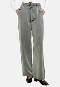 Pilkas smulkaus dryžiuko platėjantis kelnių modelis su užrišamu liemeniu ir šoninėmis kišenėmis, pagamintas iš minkštos medžiagos, derinamas su juodomis aukštakulnėmis bateliais.