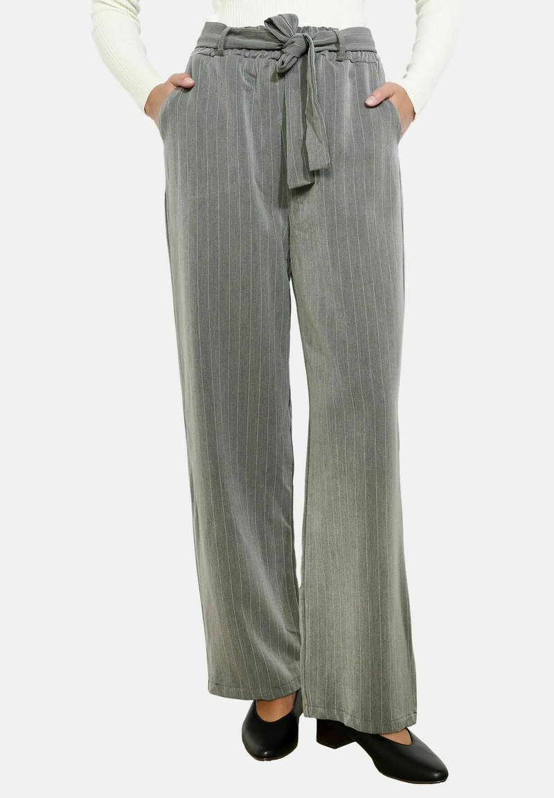 Pilkas smulkaus dryžiuko platėjantis kelnių modelis su užrišamu liemeniu ir šoninėmis kišenėmis, pagamintas iš minkštos medžiagos, derinamas su juodomis aukštakulnėmis bateliais.