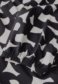 Tessuto bianco e nero con un motivo astratto che presenta forme curve. Il materiale è morbido e il bordo ha una texture arricciata.
