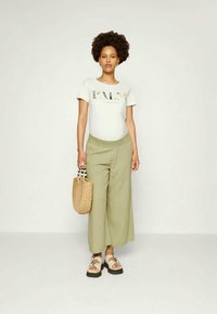 T-shirt de algodão com um design impresso, calças largas verde-azeitona, bolsa de palha trançada e sandálias grossas com uma tira padronizada.