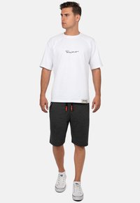 Witte t-shirt met korte mouwen en zwart scriptlogo, gecombineerd met donkergrijze shorts met een verstelbare tailleband en oranje trekkoorden. Witte schoenen.