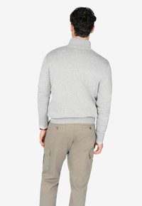 Suéter gris con un cuello alto, combinado con pantalones cargo de color beige claro que tienen bolsillos laterales y detalles de botones, visto desde la parte posterior.