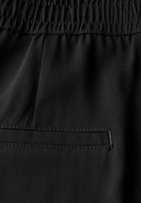 Tissu noir avec une texture lisse. Doté d'une taille élastique et d'un détail de poche cousue. Dans l'ensemble, un design minimaliste.