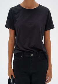 Tricou din bumbac negru cu guler rotund, mâneci scurte și croială lejeră, asortat cu blugi negri din denim și o geantă neagră.
