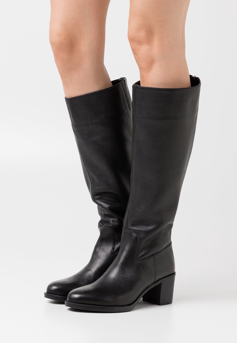 Černé kozačky ke kolenům z hladké kůže. Mají blokový podpatek a přiléhavý střih, s rovným horním okrajem a minimálním šitím.