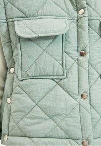 Kurtka z pikowanej tkaniny w jasnym miętowym kolorze z diamentowym wzorem. Posiada kieszeń z klapą oraz srebrne zatrzaski do zapinania. Miękka tekstura.