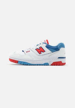 Baskets New Balance 550 blanches avec des accents rouges et bleus, col rembourré bleu, logo "N" rouge et semelle multicolore.