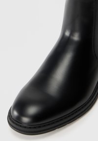 Botín de cuero negro con un acabado suave, punta redonda y un sutil tacón apilado. Presenta costuras tonales y una suela resistente.