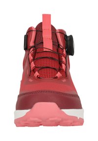 Punainen urheilushoe, jossa on verkkomateriaali, kumipohja ja integroitu nauhajärjestelmä. Varustettu erottuvalla pyöreällä nuppineulalla kiristämistä varten.