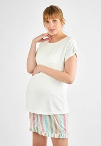 Kevyt valkoinen äitiystoppi, jossa on lyhyet hihat ja tasku, yhdistetty pastelliraidallisiin shortseihin, joissa on röyhelöreuna.