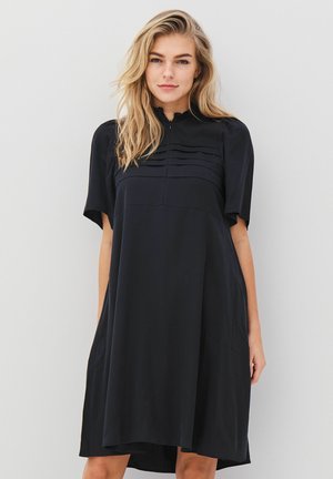 Vestido negro de mangas cortas y cuello alto, con detalles plisados en el busto. Textura suave, hasta la rodilla, ajuste relajado.