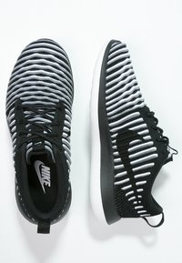 Svartvita randiga stickade sportskor med en smidig design, svart gummisula och minimal branding på sidan. Strukturerad överdel.