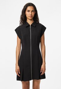 Vestido preto com um design curto e estruturado, apresentando um fecho de correr à frente e mangas curtas. Tecido suave, caimento ajustado e saia plissada.