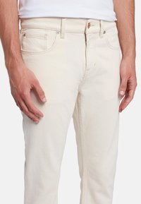 Jeans color crema chiaro con taglio dritto, realizzati in denim. Caratteristiche includono tasche frontali, zip di chiusura e dettagli in ottone.