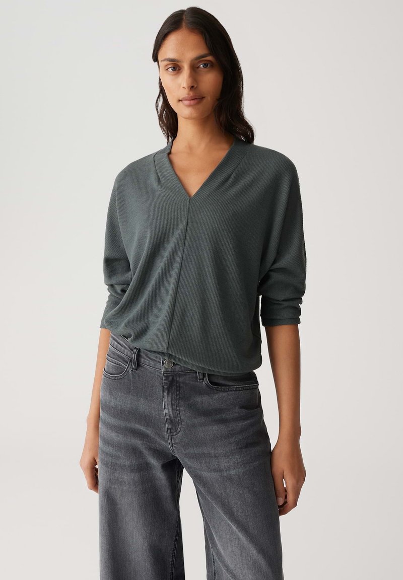 Top grigio strutturato a V con maniche ampie, abbinato a jeans a gamba larga grigio scuro. Design semplice, che enfatizza il comfort e lo stile casual.