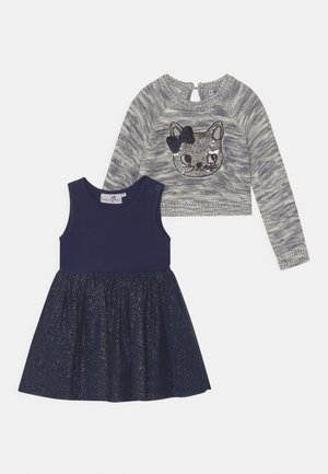 Granatowa sukienka bez rękawów z błyszczącą spódnicą oraz szary dziany sweter z długim rękawem, ozdobiony cekinową twarzą kota i granatową kokardką.